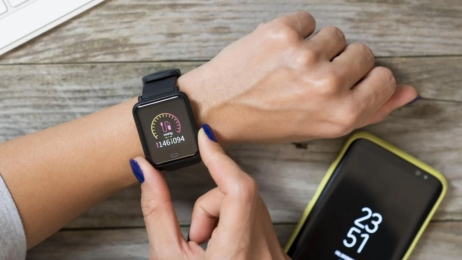 Woman measuring blood pressure with modern smart watch against wooden table
