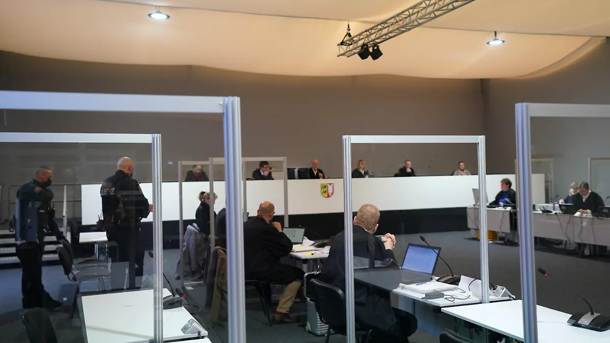 07.03.2022, Schleswig-Holstein, Kiel: Der Angeklagte (verdeckt) sitzt zu Beginn des Prozesstages wegen eines Dreifachmordes im Sitzungssaal der Außenstelle des Landgerichts Kiel neben seiner Anwältin und seinem Anwalt. Am 19. Mai 2021 soll der Mann zuerst seine von ihm getrennt lebende Ehefrau und deren neuen Bekannten in Dänischenhagen mit einer Maschinenpistole erschossen und danach in Kiel einen gemeinsamen Bekannten des Ehepaares mit einer halbautomatischen Pistole getötet haben. Mit der zweiten Waffe stellte er sich am Abend in Hamburg der Polizei. Foto: Marcus Brandt/dpa +++ dpa-Bildfunk +++