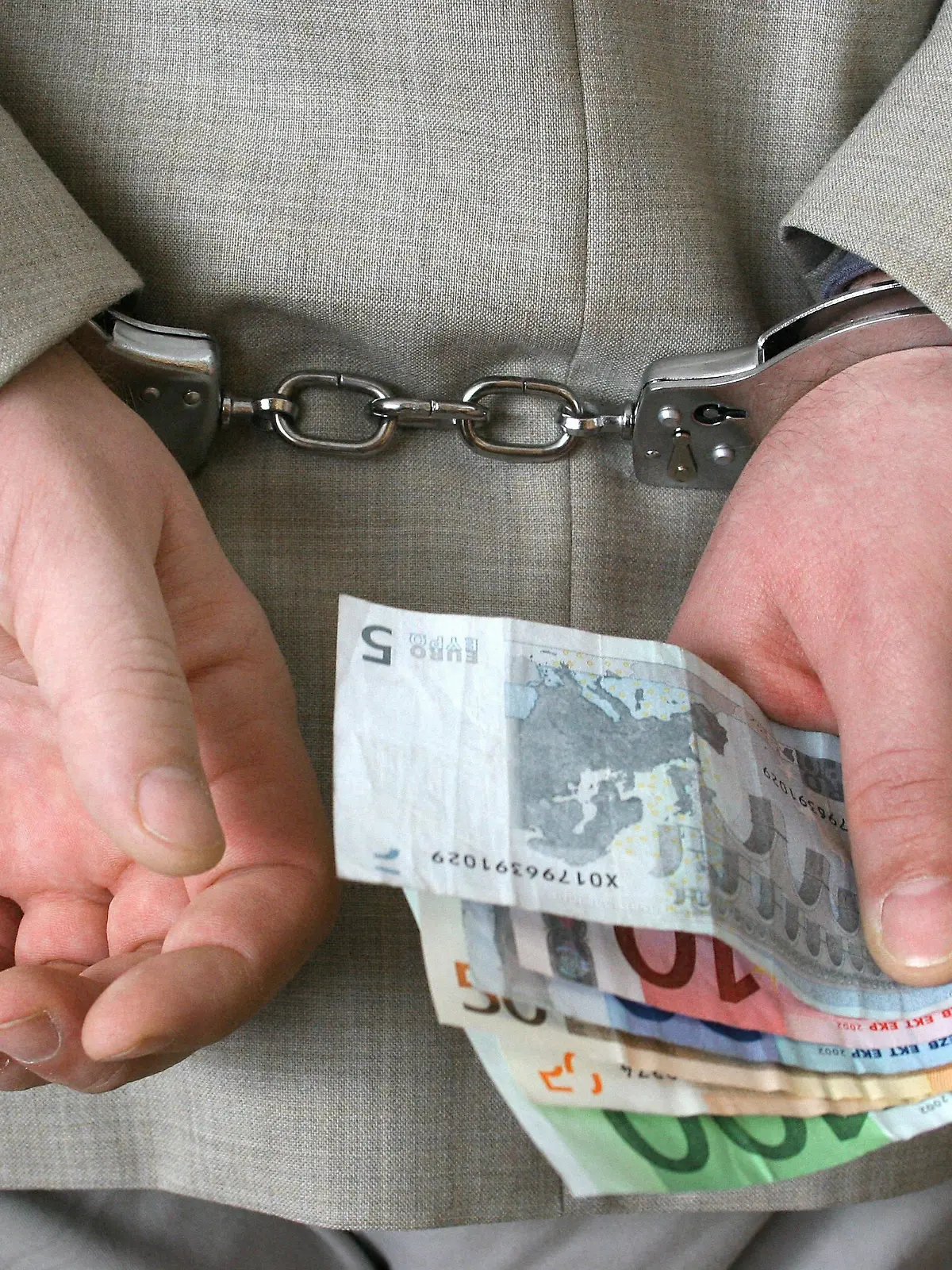Geschaeftsmann in Handschellen haelt Geldscheine in einer Hand | handcuffed businessman holding Euro bills in his hand