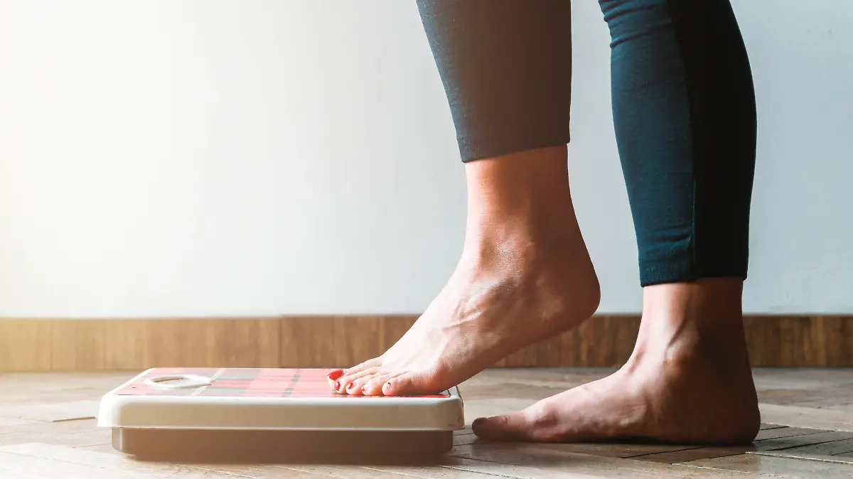 Female checking kilogrammes getting on the scale - self care and body positivity concept - warm flare on left