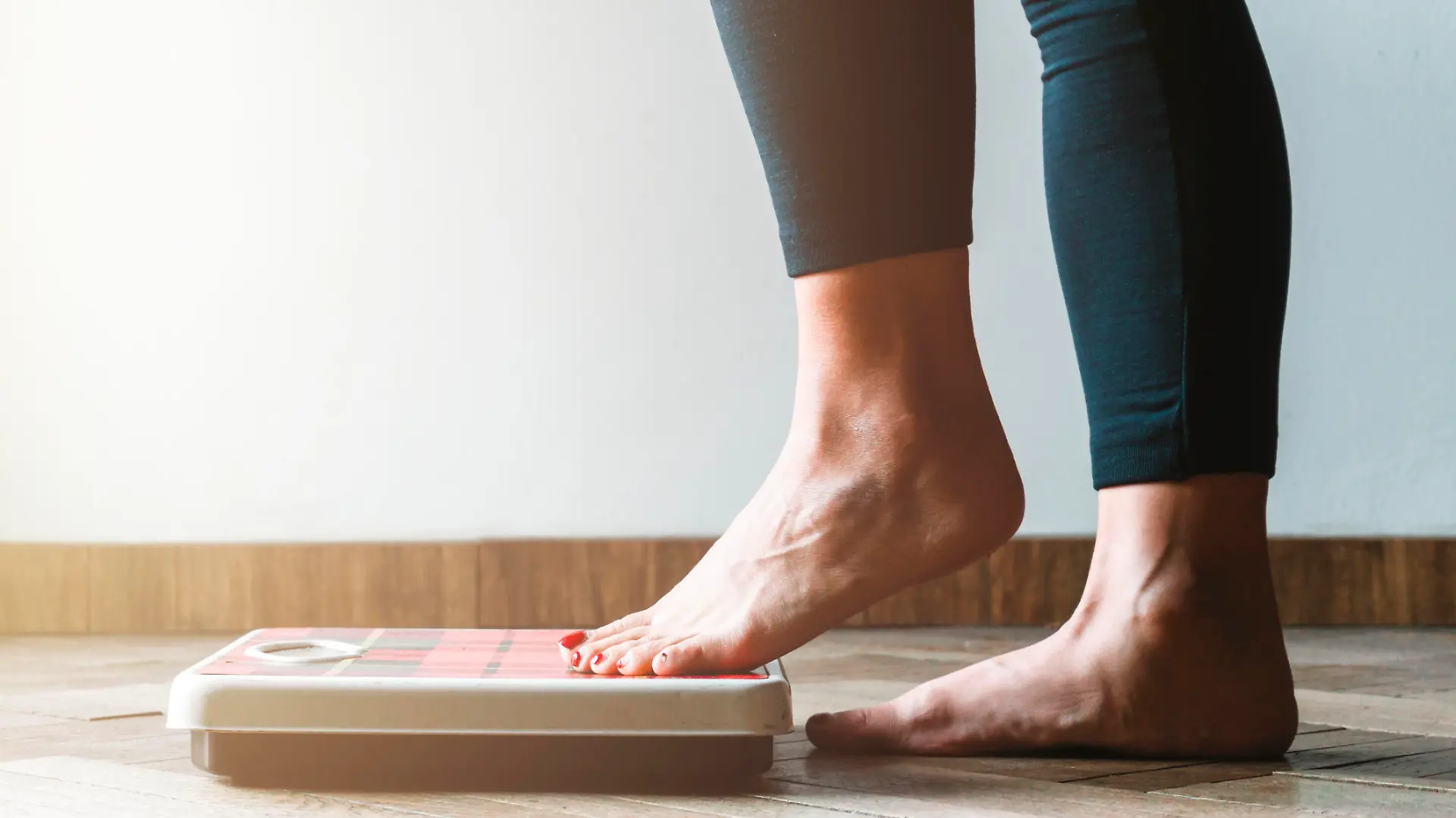 Female checking kilogrammes getting on the scale - self care and body positivity concept - warm flare on left