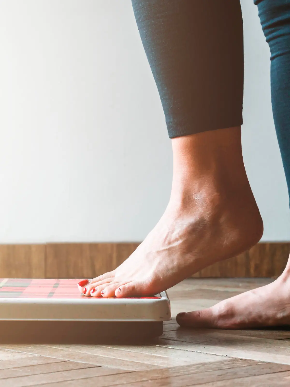 Female checking kilogrammes getting on the scale - self care and body positivity concept - warm flare on left