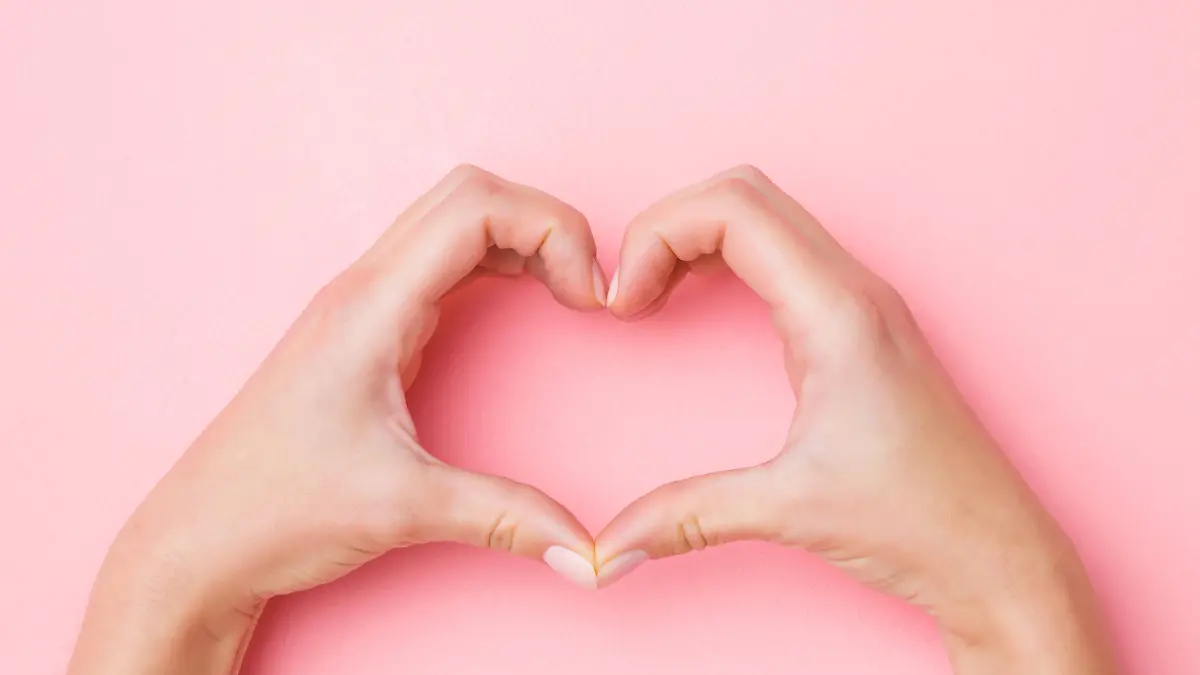 Heart shape created from young woman's hands on pastel pink background. Love and happiness concept. Empty place for emotional, sentimental text, quote or sayings. Closeup.