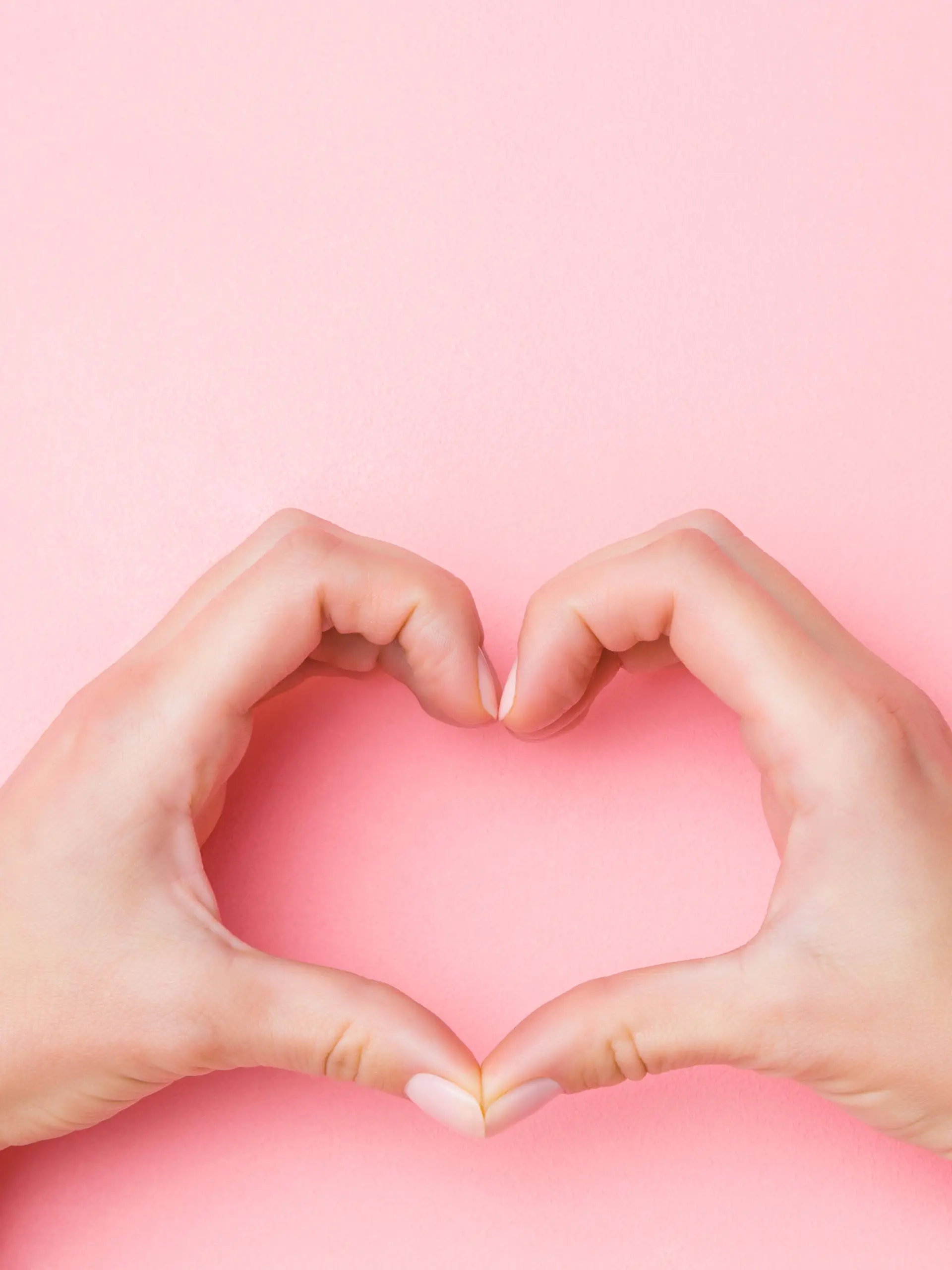Heart shape created from young woman's hands on pastel pink background. Love and happiness concept. Empty place for emotional, sentimental text, quote or sayings. Closeup.