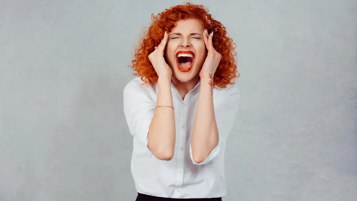 Screaming stressed. Portrait frustrated shocked redhead business woman yelling eyes closed hands on head temper tantrum isolated grey wall background. Negative human emotion facial expression reaction
