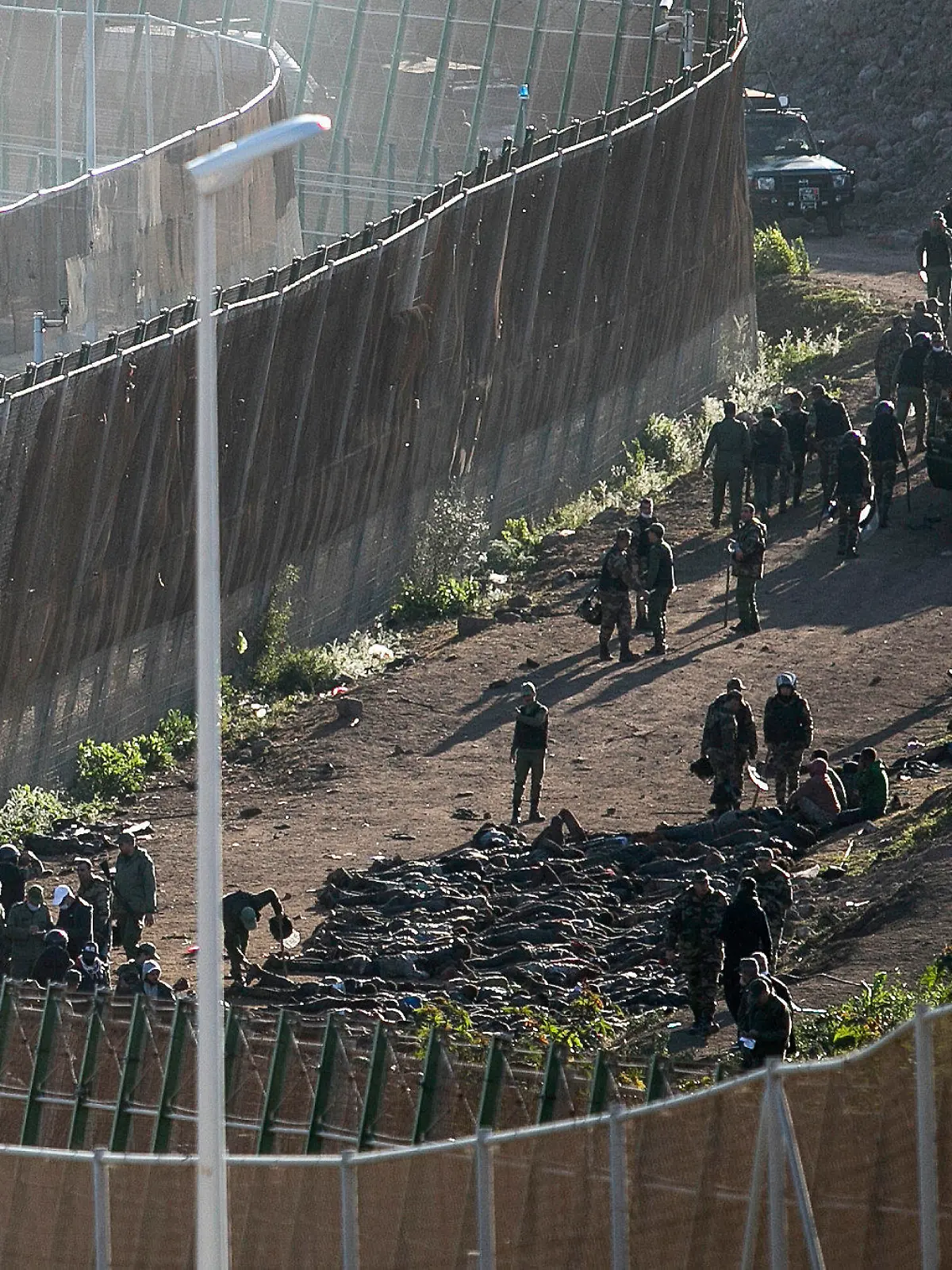 03.03.2022, Spanien, Melilla: Sicherheitskräfte auf der marokkanischen Seite der Grenze zwingen Migranten, sich vor den Zaun zu legen, nachdem sie sie daran gehindert haben, die Zäune zwischen der spanischen autonomen Stadt Melilla in Nordafrika und Marokko zu überwinden. Nach Angaben der Beamten in Melilla haben mehrere Hundert Migranten die Zäune überquert, die Melilla von Marokko trennen. Foto: Javier Bernardo/AP/dpa +++ dpa-Bildfunk +++