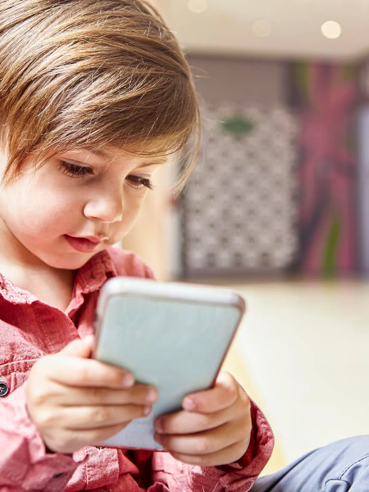 Portrait of little boy sitting on the floor while using smart phone at mall during daytime