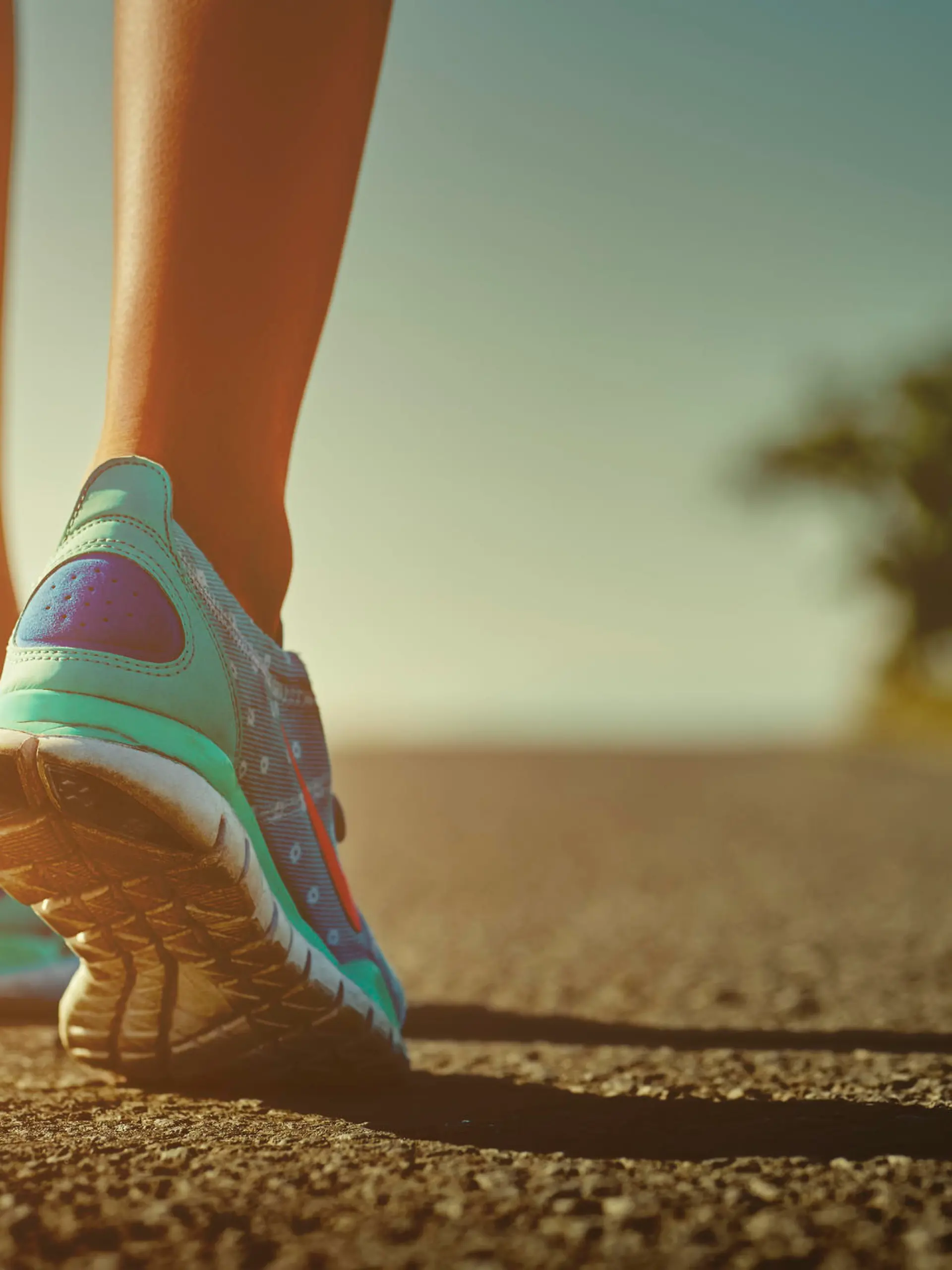 Closeup of female runner shaved feet in running shoes going for a run on the road at sunrise or sunset. Shallow depth of field, toned with instagram like filter, flare effect.