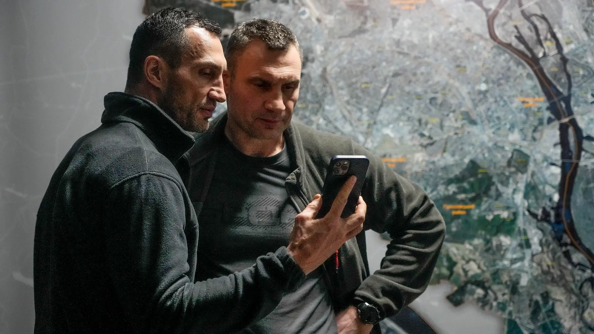 dpatopbilder - 27.02.2022, Ukraine, Kiew: Vitali Klitschko (r), Bürgermeister von Kiew und ehemaliger Box-Profi, und sein Bruder Wladimir Klitschko, ebenfalls ehemaliger Box-Profi, schauen auf ein Smartphone im Rathaus in Kiew. Russische Truppen haben den erwarteten Angriff auf die Ukraine gestartet und drangen in die Hauptstadt vor. Foto: Efrem Lukatsky/AP/dpa +++ dpa-Bildfunk +++