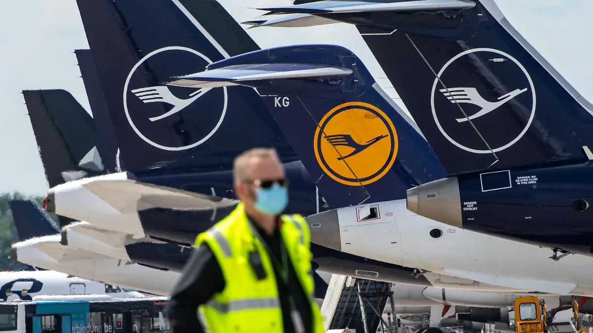 ARCHIV - 03.06.2020, Bayern, München: Ein Mann mit Mundschutzmaske steht vor Lufthansa-Maschinen, die nebeneinander am Terminal des Flughafens stehen. (Zu dpa "Lufthansa streicht noch mehr Flieger und Jobs") Foto: Peter Kneffel/dpa +++ dpa-Bildfunk +++