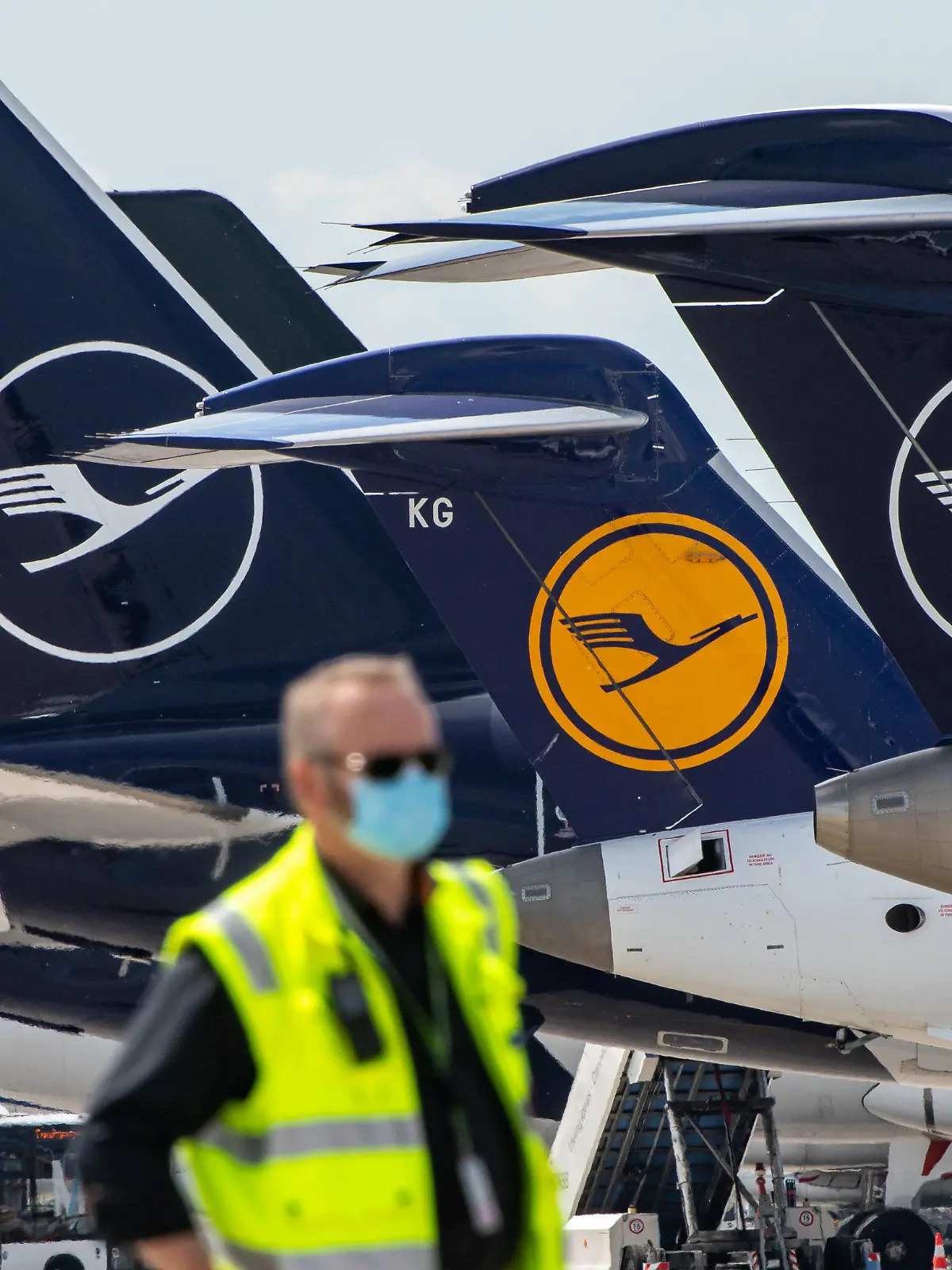 ARCHIV - 03.06.2020, Bayern, München: Ein Mann mit Mundschutzmaske steht vor Lufthansa-Maschinen, die nebeneinander am Terminal des Flughafens stehen. (Zu dpa "Lufthansa streicht noch mehr Flieger und Jobs") Foto: Peter Kneffel/dpa +++ dpa-Bildfunk +++