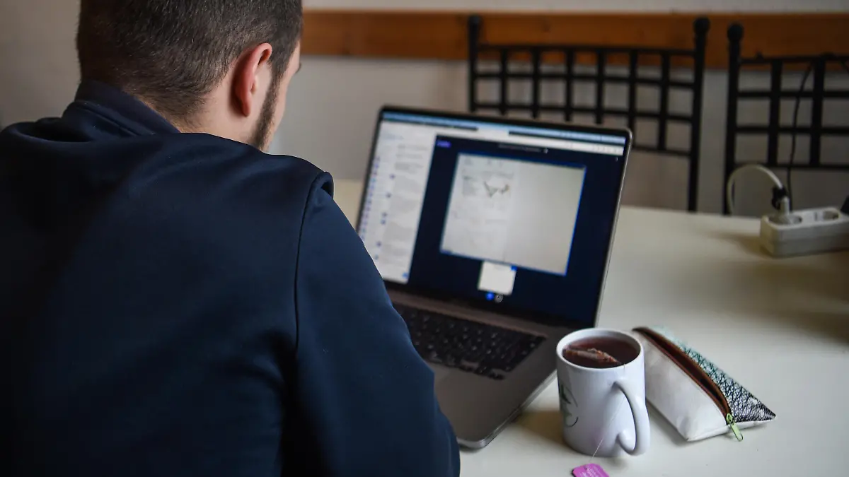 Ein junger Mann sitzt an seinem Esstisch in der Küche und nimmt an einer Online-Vorlesung seiner Hochschule teil. Aufgrund der Virusmutation sollen schon kommende Woche über neue verschärfte Maßnahmen beraten werden.