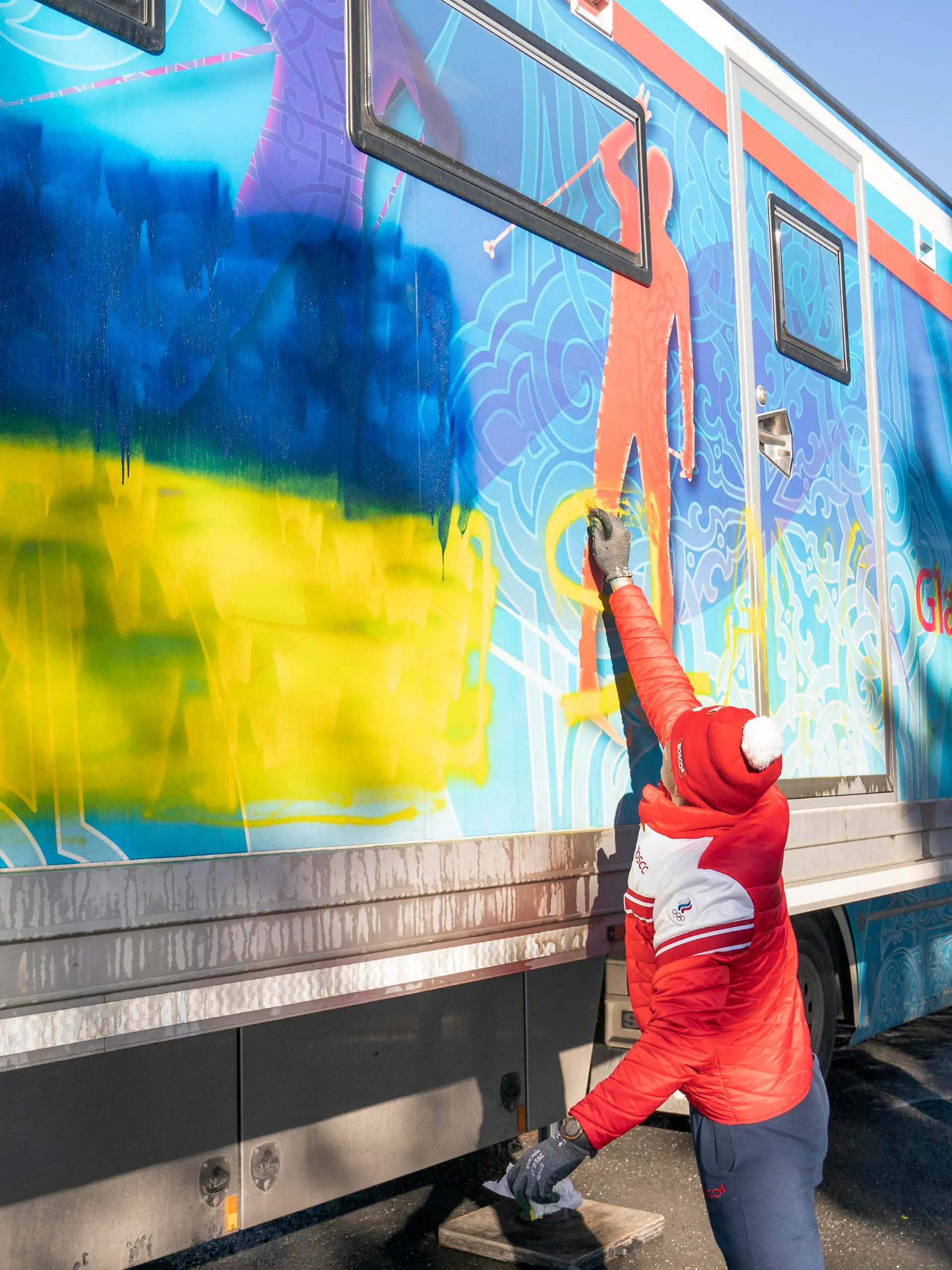 02.03.2022, Norwegen, Oslo: Mitglieder der russischen Langlauf-Nationalmannschaft versuchen, eine ukrainische Flagge und den Schriftzug «Ruhm für die Ukraine» von der Seite des Anhängers der russischen Langlauf-Nationalmannschaft am Holmenkollen in der Nähe von Oslo zu entfernen. In Norwegen waren die russischen Langläufer, die bei den Olympischen Spielen in Peking 11 Medaillen gewonnen hatten, auf dem Heimweg, nachdem sie vom Internationalen Skiverband (FIS) vom Wettbewerb ausgeschlossen worden waren. Die Entscheidung fiel nach einem dreitägigen Patt mit norwegischen Skifunktionären, die sich weigerten, Sportler aus Russland und Belarus an den Start zu schicken, wenn die FIS an ihrer bisherigen Politik festhält, sie als neutrale Athleten antreten zu lassen. Foto: Torstein Boee/NTB Norway/AP/dpa +++ dpa-Bildfunk +++