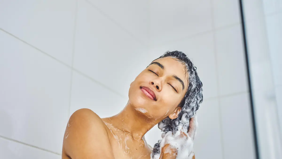 Shot of an attractive young woman washing her hair with shampoo in the shower at home