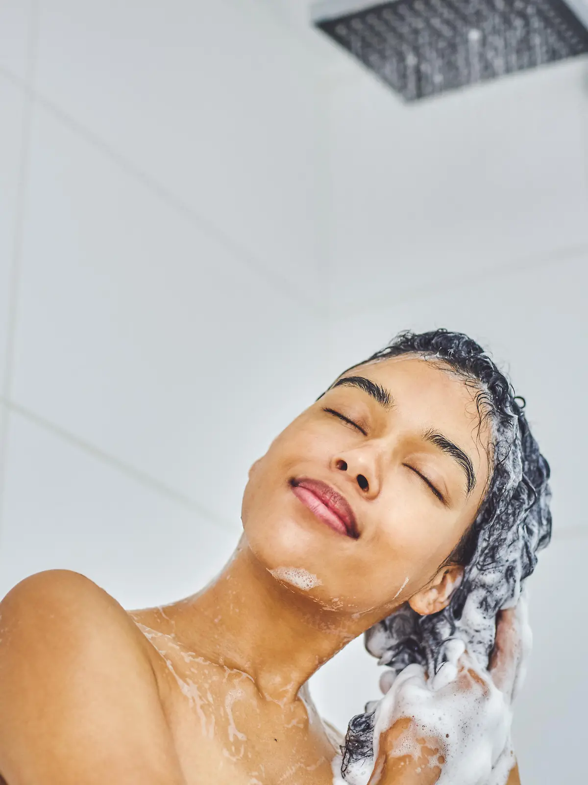 Shot of an attractive young woman washing her hair with shampoo in the shower at home