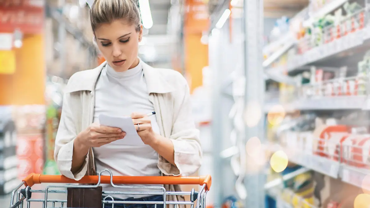 Closeup front view of late 20's woman at a local supermarket checking her shopping list while going through aisles. There are many unrecognizable products on the shelves next to her and in background.