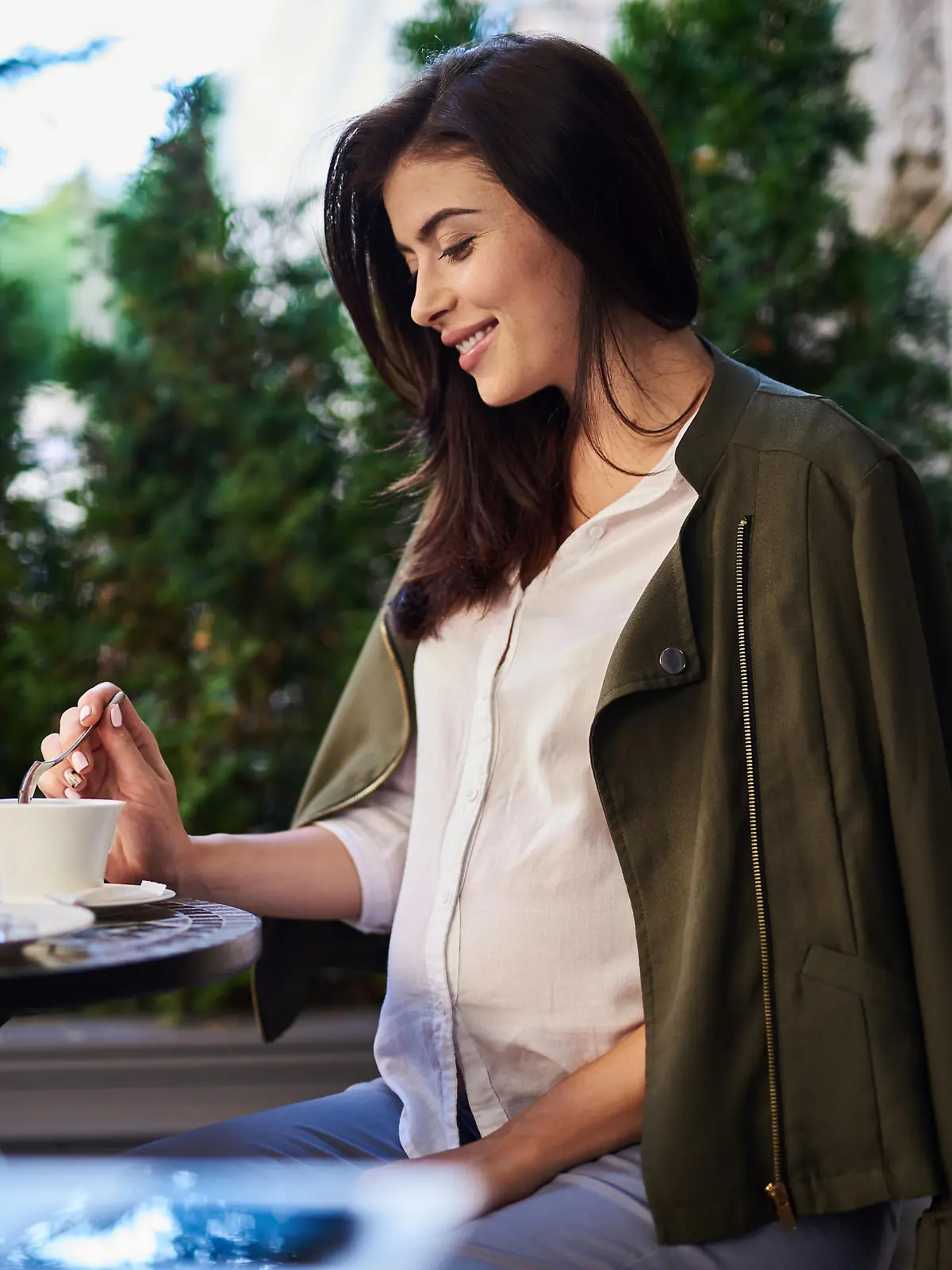 Eine schwangere Frau sitzt mit einem Getränk außerhalb eines Cafés.
