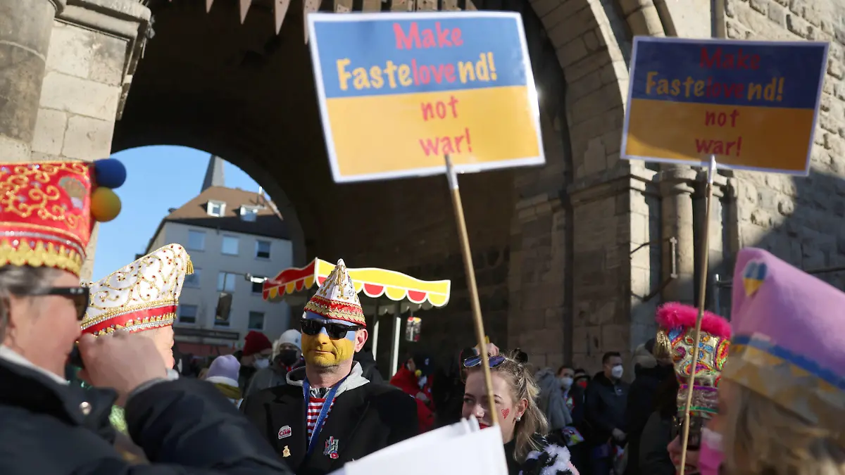 28.02.2022, Nordrhein-Westfalen, Köln: Karnevalisten haben sich mit Schildern mit der Aufschrift "Make Fastelovend ! Not war !" bei der Friedensdemonstration am Rosenmontag am Severinstor versammelt. Nach dem russischen Angriff auf die Ukraine wurde das Rosenmontagsfest abgesagt, stattdessen zieht ein Protestmarsch durch die Innenstadt - vorbei an vielen der Motivwagen, die eigentlich für den Rosenmontagszug gebaut worden waren. Foto: Oliver Berg/dpa +++ dpa-Bildfunk +++