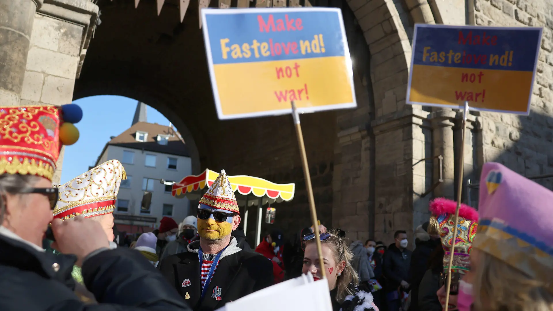 28.02.2022, Nordrhein-Westfalen, Köln: Karnevalisten haben sich mit Schildern mit der Aufschrift "Make Fastelovend ! Not war !" bei der Friedensdemonstration am Rosenmontag am Severinstor versammelt. Nach dem russischen Angriff auf die Ukraine wurde das Rosenmontagsfest abgesagt, stattdessen zieht ein Protestmarsch durch die Innenstadt - vorbei an vielen der Motivwagen, die eigentlich für den Rosenmontagszug gebaut worden waren. Foto: Oliver Berg/dpa +++ dpa-Bildfunk +++