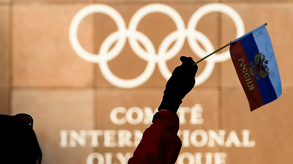 Eine Frau hält am 05.12.2017 eine russische Fahne vor den olympischen Ringen am Hauptquartierdes Internationalen Olympischen Komitees (IOC) in Lausanne (Schweiz). Das IOC wollte im Laufe des Tages über Strafen bis hin zu einem Ausschluss der Sport-Großmacht Russland von den Olympischen Winterspielen im Februar in Südkorea beraten. Möglich ist auch ein Verbot russischer Symbole wie der Fahne und der Hymne Foto: Jean-Christophe Bott/KEYSTONE/dpa +++(c) dpa - Bildfunk+++