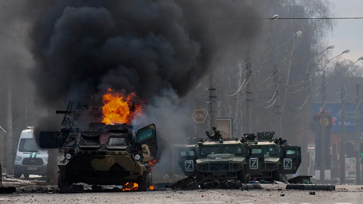 dpatopbilder - 27.02.2022, Ukraine, Charkiw: Ein gepanzerter Mannschaftswagen brennt und beschädigte Nutzfahrzeuge stehen nach Kämpfen in Charkiw auf einer Straße, während eine anscheinend leblose Person auf der Straße liegt. Wegen des russischen Angriffs auf die Ukraine sind nach Angaben des UN-Flüchtlingshilfswerks (UNHCR) etwa 368 000 Menschen auf der Flucht. Foto: Marienko Andrew/AP/dpa +++ dpa-Bildfunk +++
