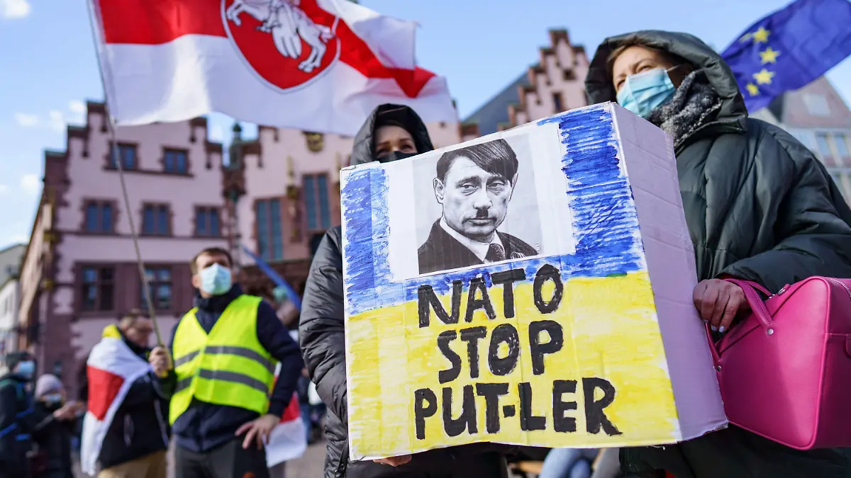 27.02.2022, Hessen, Frankfurt/Main: Demonstrantinnen halten ein Plakat mit der Aufschrift "Nato stop Put-ler" mit dem Bild eines Gesichts, das eine Mischung von Hitler und Putin darstellt, bei einer Kundgebung auf dem Römerberg für Frieden in der Ukraine und gegen den russischen Einmarsch. «Putler» ist eine Wortschöpfung aus den Namen «Putin» und «Hitler». Foto: Frank Rumpenhorst/dpa +++ dpa-Bildfunk +++
