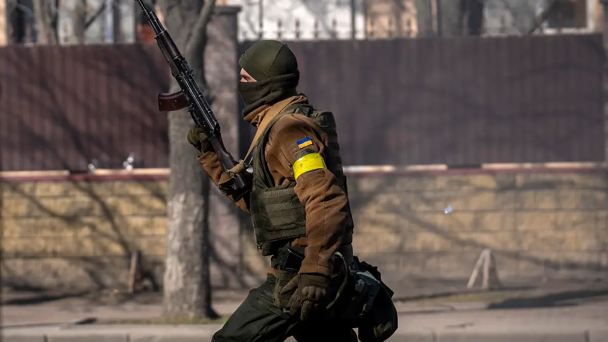 26.02.2022, Ukraine, Kiew: Ein ukrainischer Soldat geht mit seiner Waffe in der Hand vor einer Militäreinrichtung. Russische Truppen haben den erwarteten Angriff auf die Ukraine gestartet und drangen in die Hauptstadt vor. Foto: Emilio Morenatti/AP/dpa +++ dpa-Bildfunk +++