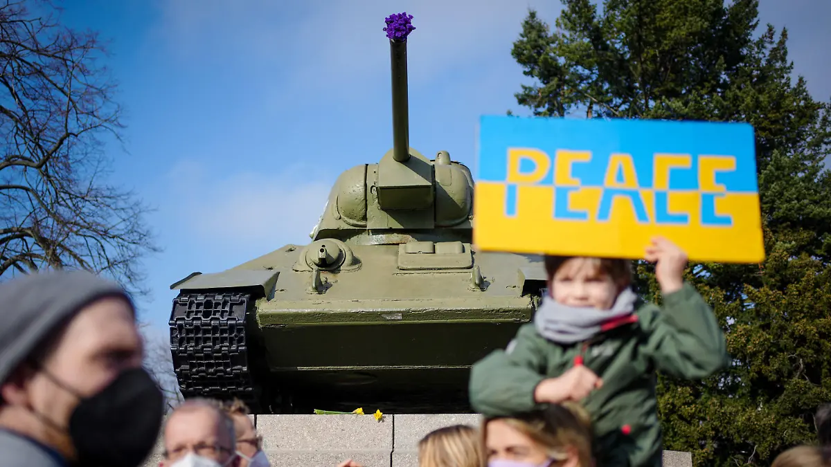 27.02.2022, Berlin: Teilnehmer demonstrieren mit einem Schild mit der Aufschrift «Peace» darauf an der Gedenkstätte für die getöteten sowjetischen Soldaten im Zweiten Weltkrieg vor einem sowjetischen Panzer vom Typ T34 gegen den Krieg in der Ukraine. Foto: Kay Nietfeld/dpa +++ dpa-Bildfunk +++