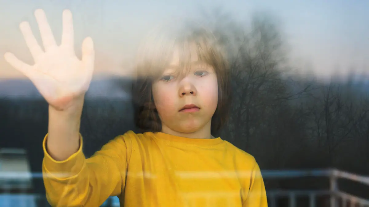 Kind steht traurig am Fenster