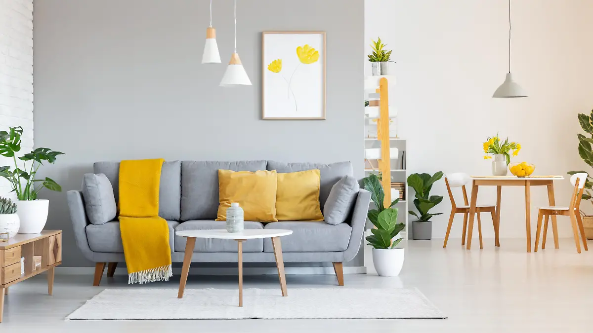 Orange blanket on grey sofa in modern apartment interior with poster and wooden table. Real photo