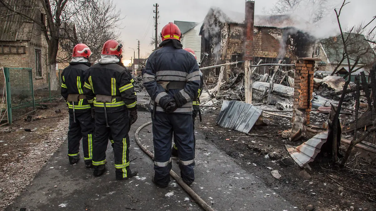25.02.2022, Ukraine, Kiew: Feuerwehrleute betrachten die Trümmer eines Flugzeugs das zwischen Häusern abgestürzt ist. Es war unklar, wessen Flugzeug abgestürzt ist und wer es zum Absturz gebracht hat. Russische Truppen sollen bis in die Außenbezirke der Hauptstadt vorgedrungen sein. Russland hat am Donnerstag einen umfassenden Angriff auf die Ukraine gestartet und Städte und Stützpunkte mit Luftangriffen oder Granaten beschossen. Foto: Oleksandr Ratushniak/AP/dpa +++ dpa-Bildfunk +++
