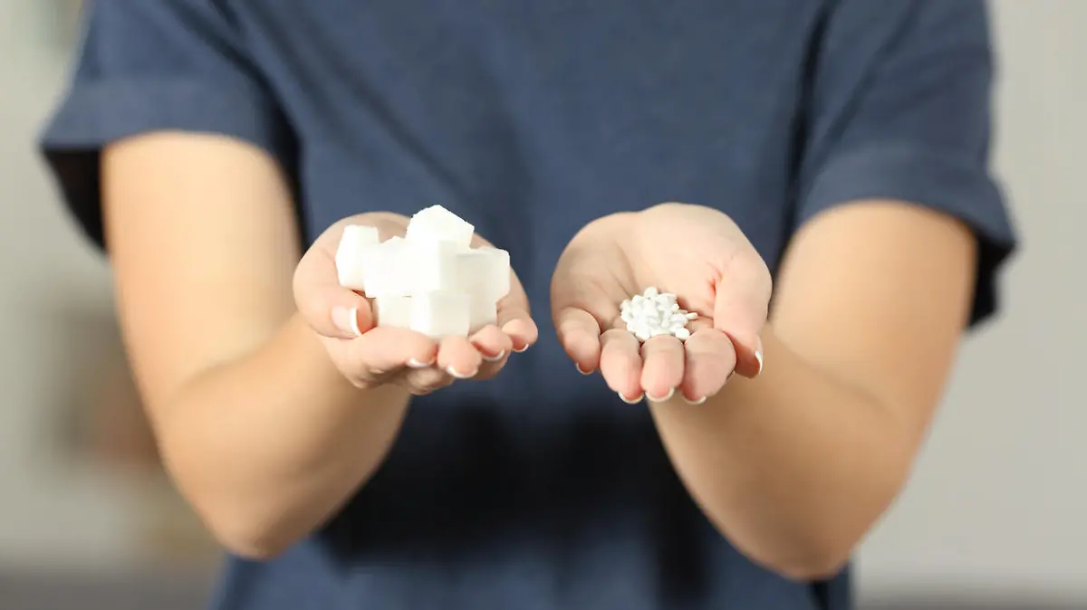 Front view close up of a woman hands holding sugar cubes and saccharin pills at home