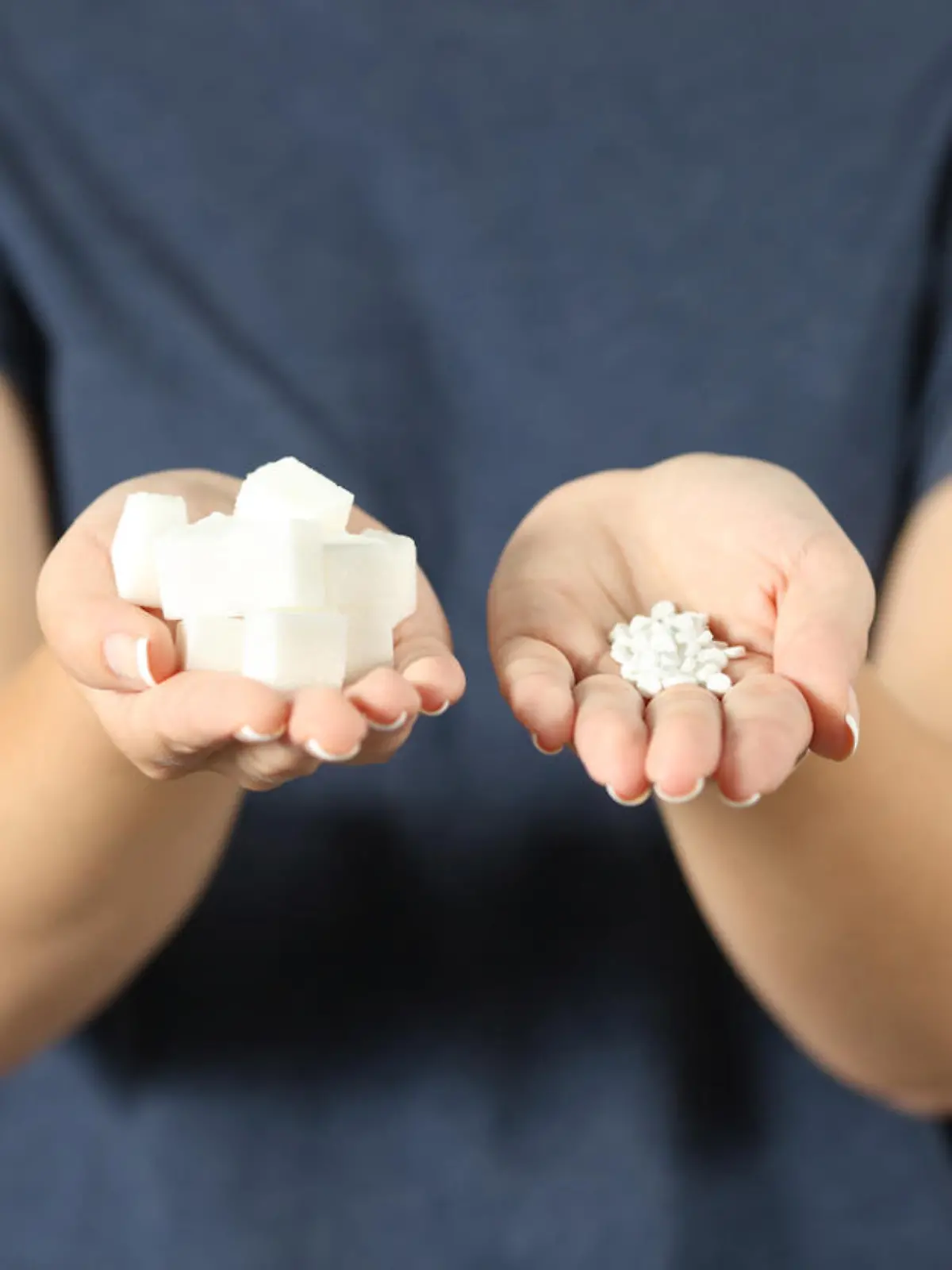 Front view close up of a woman hands holding sugar cubes and saccharin pills at home