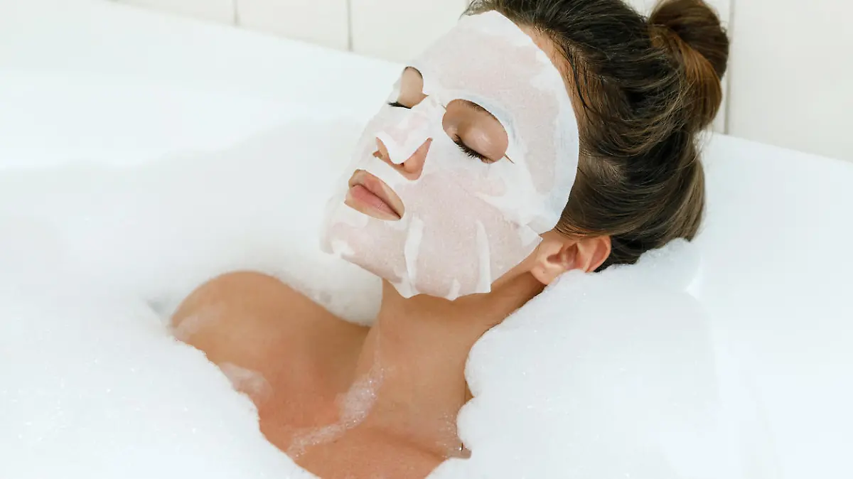 Woman lying in bathtub with a sheet mask on her face