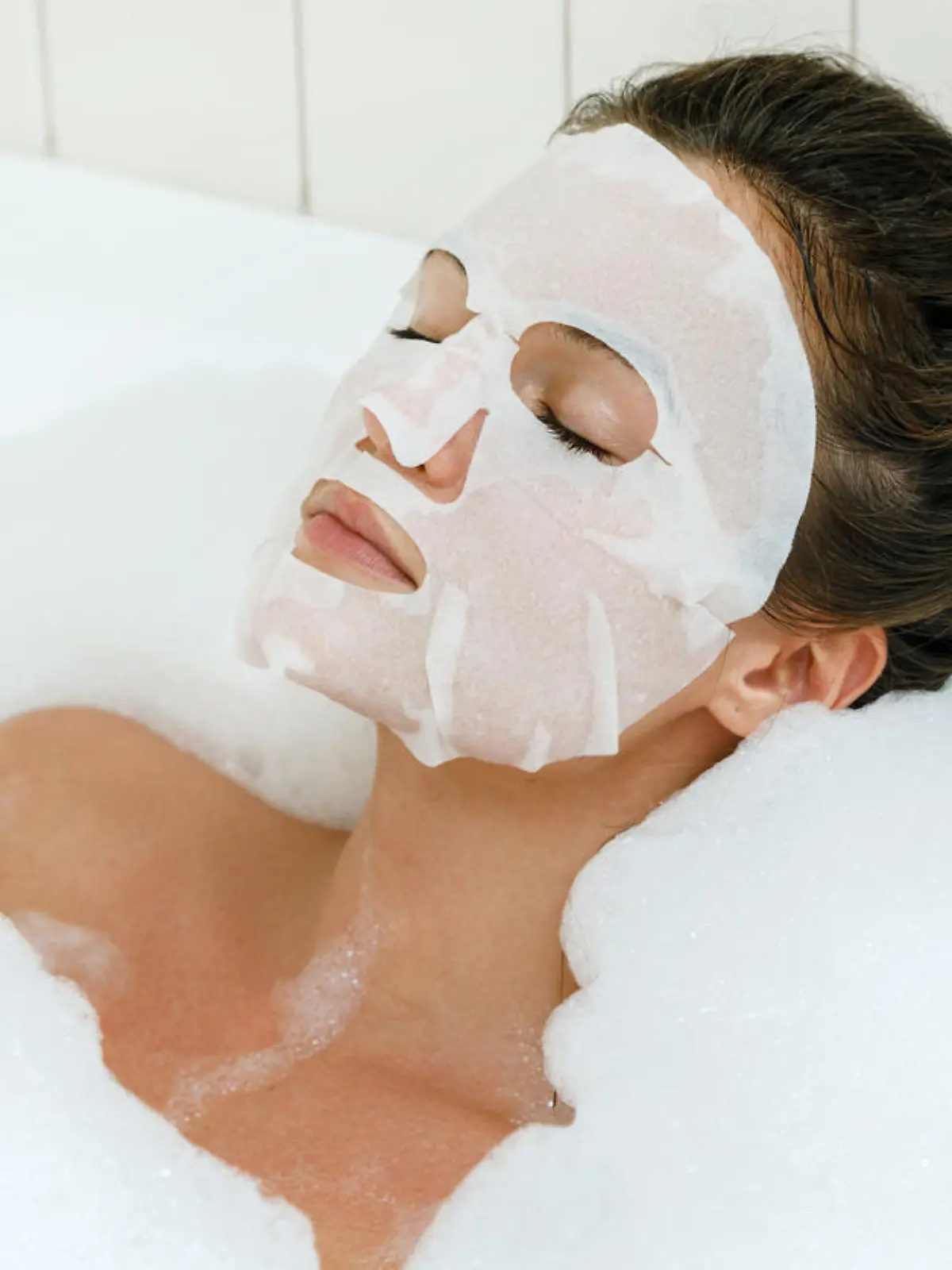 Woman lying in bathtub with a sheet mask on her face