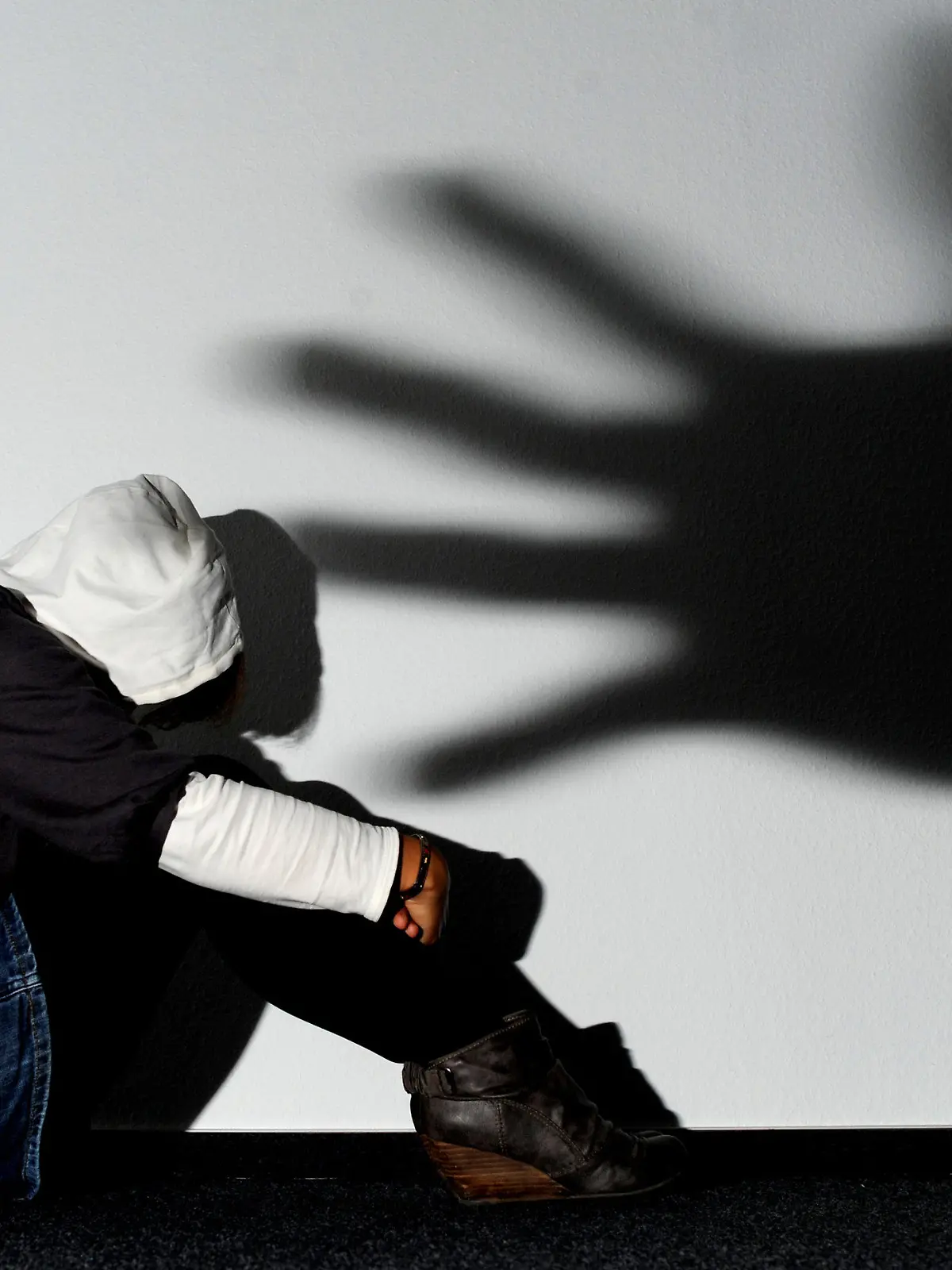 ARCHIV - ILLUSTRATION - Ein Mädchen sitzt am 14.09.2011 vor einer Wand in Hannover, auf der der Schatten einer Hand groß zu sehen ist (Symbolbild zum Thema Opfer von Gewalttaten). Opfer schwerer Straftaten in Niedersachsen sollen eine bessere Unterstützung erhalten. Unter anderem wird landesweit das Angebot der psychosozialen Prozessbegleitung auf den Weg gebracht. Foto: Julian Stratenschulte dpa/lni (zu lni 0302 vom 11.09.2012)  +++(c) dpa - Bildfunk+++