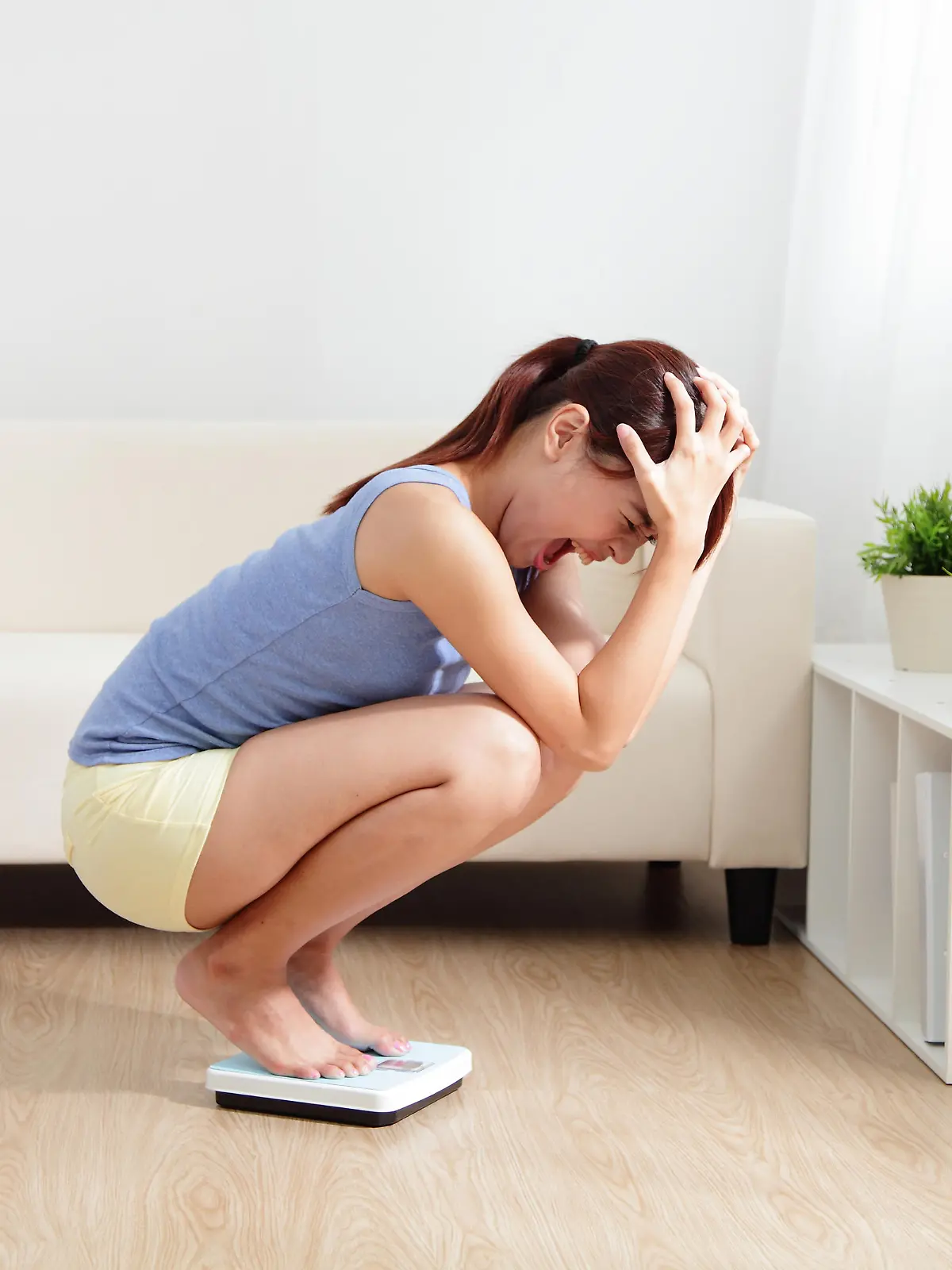 Upset woman on weigh scale at home, asian