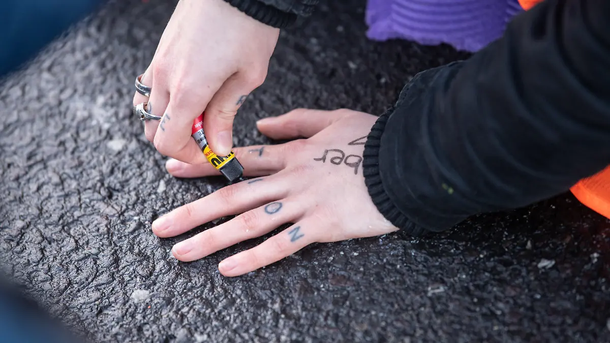 23.02.2022, Hessen, Frankfurt/Main: Aktivisten der ·Letzten Generationen· blockieren den Airportring am Flughafen Frankfurt. Eine Aktivistin klebt ihre Hand mit Sekundenkleber am Asphalt fest. Foto: Boris Roessler/dpa +++ dpa-Bildfunk +++