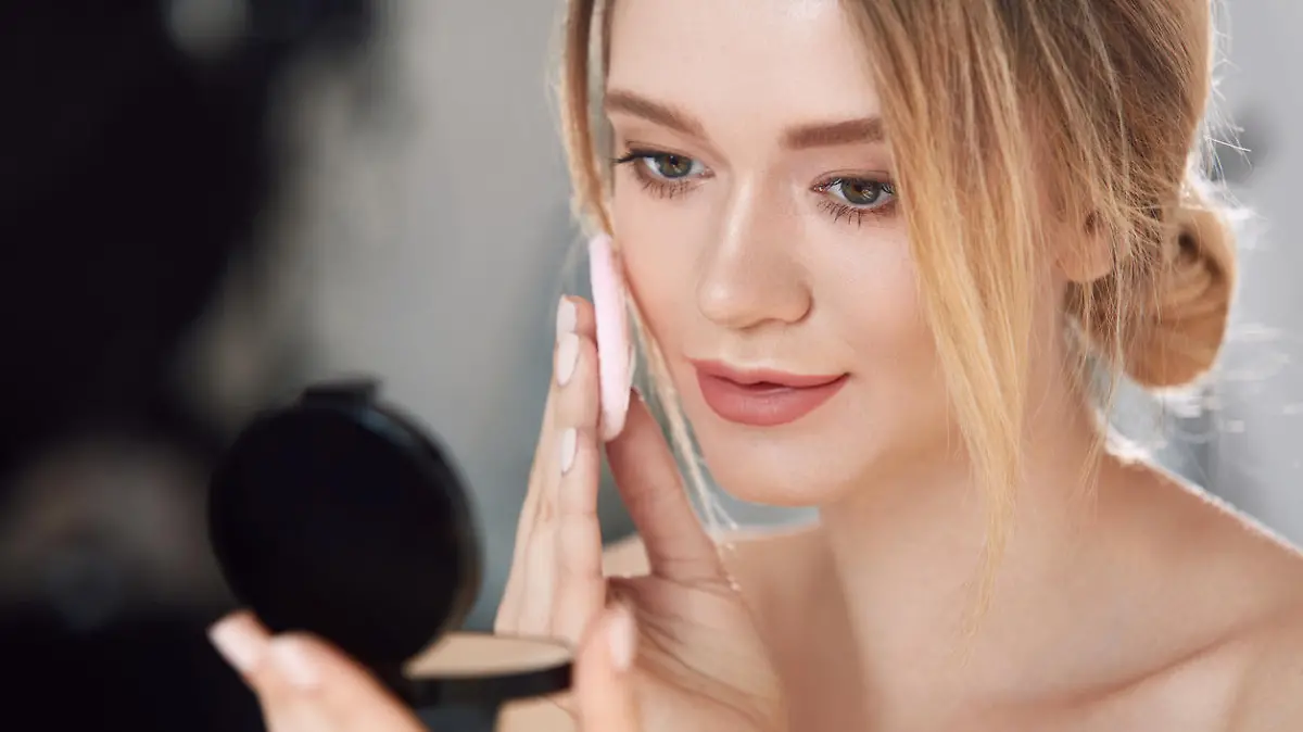 Face Make-Up. Closeup Of Sexy Female Applying Dry Powder Foundation Looking In Mirror. Portrait Of Young Woman Putting Makeup Powder With Cosmetic Cushion On Her Facial Skin Indoors. High Resolution