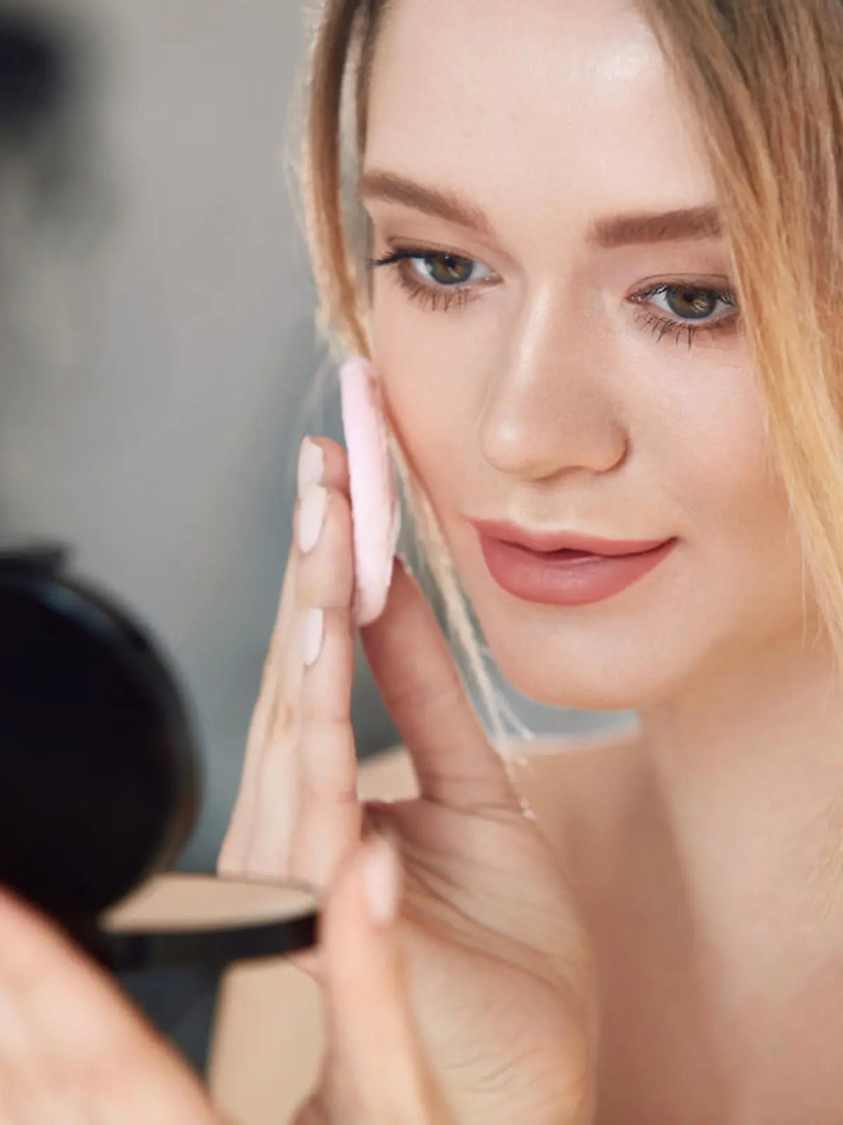 Face Make-Up. Closeup Of Sexy Female Applying Dry Powder Foundation Looking In Mirror. Portrait Of Young Woman Putting Makeup Powder With Cosmetic Cushion On Her Facial Skin Indoors. High Resolution