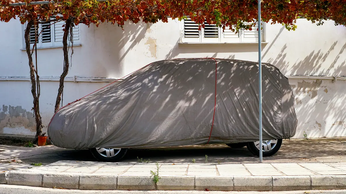 Car under gray textile cover outside.