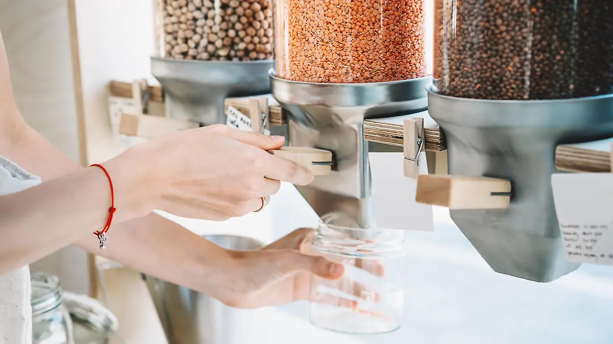 Sustainable shopping at small local businesses. Close-up image of woman pours red lentils in glass jar from dispensers in plastic free grocery store. Girl with cotton bag buying in zero waste shop.