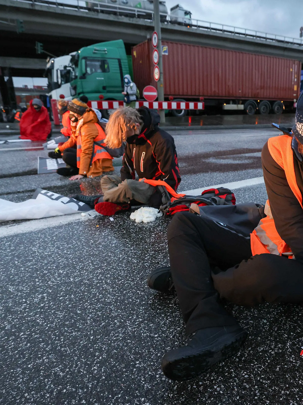 21.02.2022, Hamburg: Klimaaktivisten der Aktion ·Aufstand der letzten Generation· blockieren am Morgen eine Kreuzung am Zollamt Waltershof zur Köhlbrandbrücke und zur Autobahn A7. Einige Aktivisten kleben sich mit Sekundenkleber und Bauschaum an der Fahrbahn fest. Foto: Christian Charisius/dpa +++ dpa-Bildfunk +++