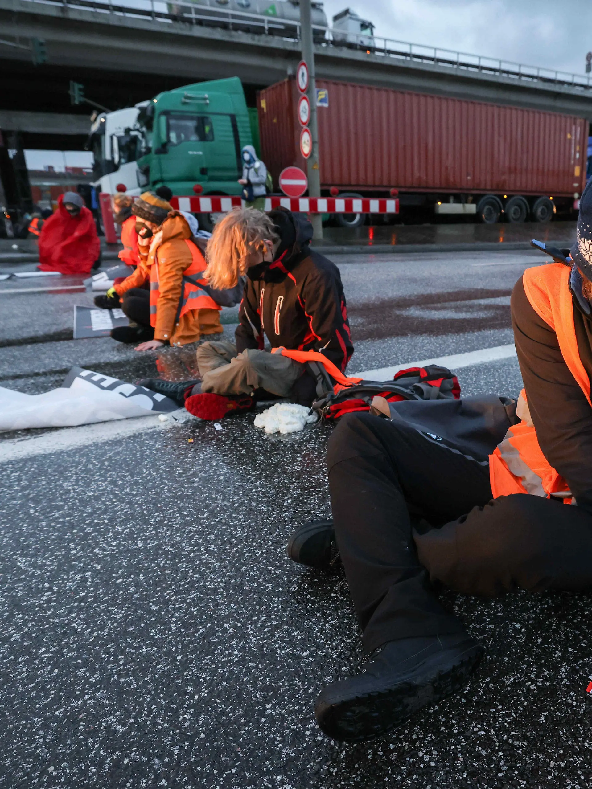 21.02.2022, Hamburg: Klimaaktivisten der Aktion ·Aufstand der letzten Generation· blockieren am Morgen eine Kreuzung am Zollamt Waltershof zur Köhlbrandbrücke und zur Autobahn A7. Einige Aktivisten kleben sich mit Sekundenkleber und Bauschaum an der Fahrbahn fest. Foto: Christian Charisius/dpa +++ dpa-Bildfunk +++
