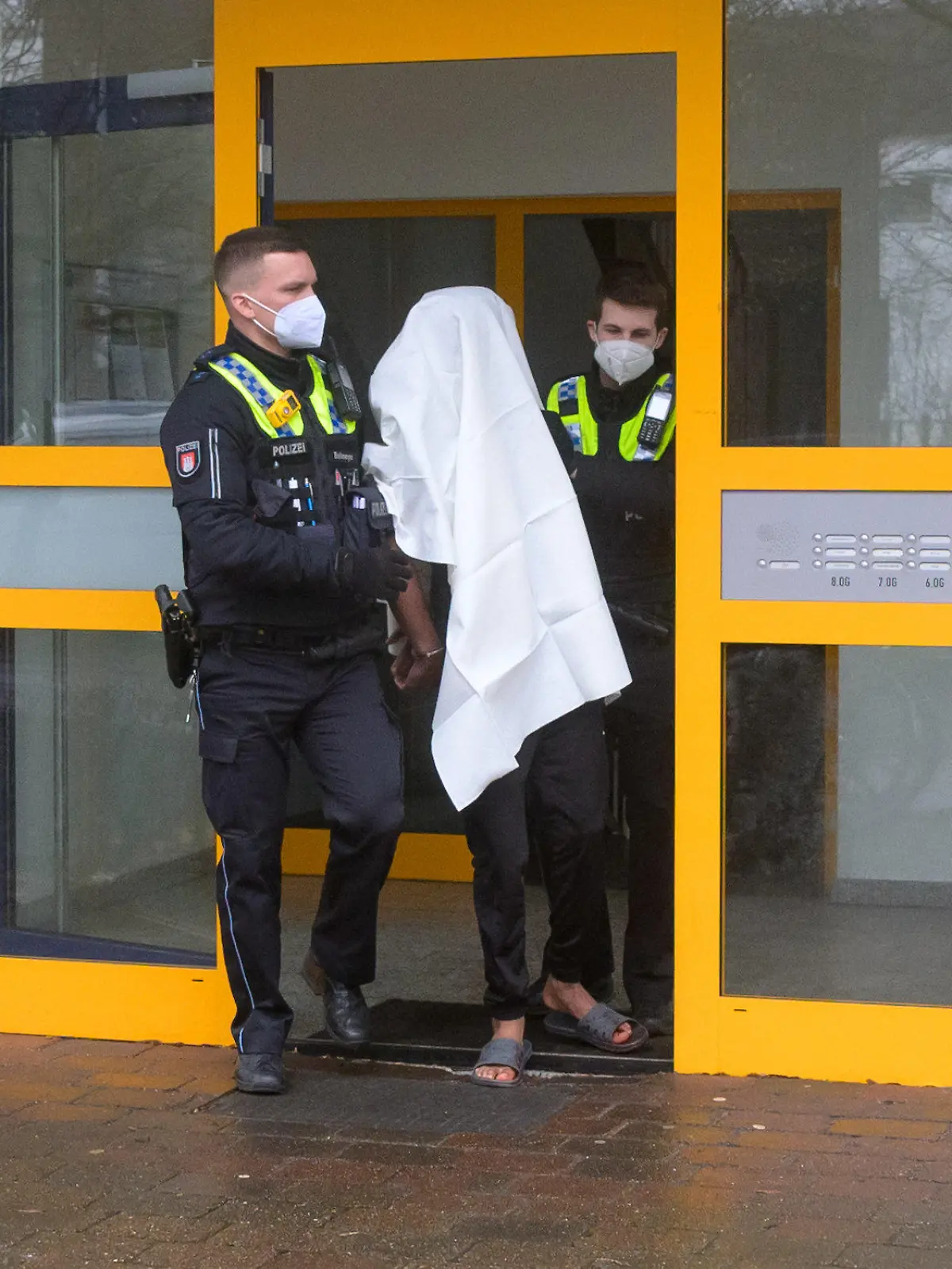 20.02.2022, Hamburg: Polizisten führen einen Tatverdächtigen in Handschellen aus dem Haus. Eine Frau ist am Sonntag mit lebensgefährlichen Stichverletzungen in Hamburg-Niendorf aufgefunden worden. Nach Angaben eines Sprechers hatte eine Anwohnerin Blut im Hausflur gesehen und die Einsatzkräfte verständigt. Den ersten Angaben zufolge sei von einer Auseinandersetzung die Rede gewesen, bei der eine Frau mit einem Messer verletzt worden sei. Foto: Jonas Walzberg/dpa +++ dpa-Bildfunk +++
