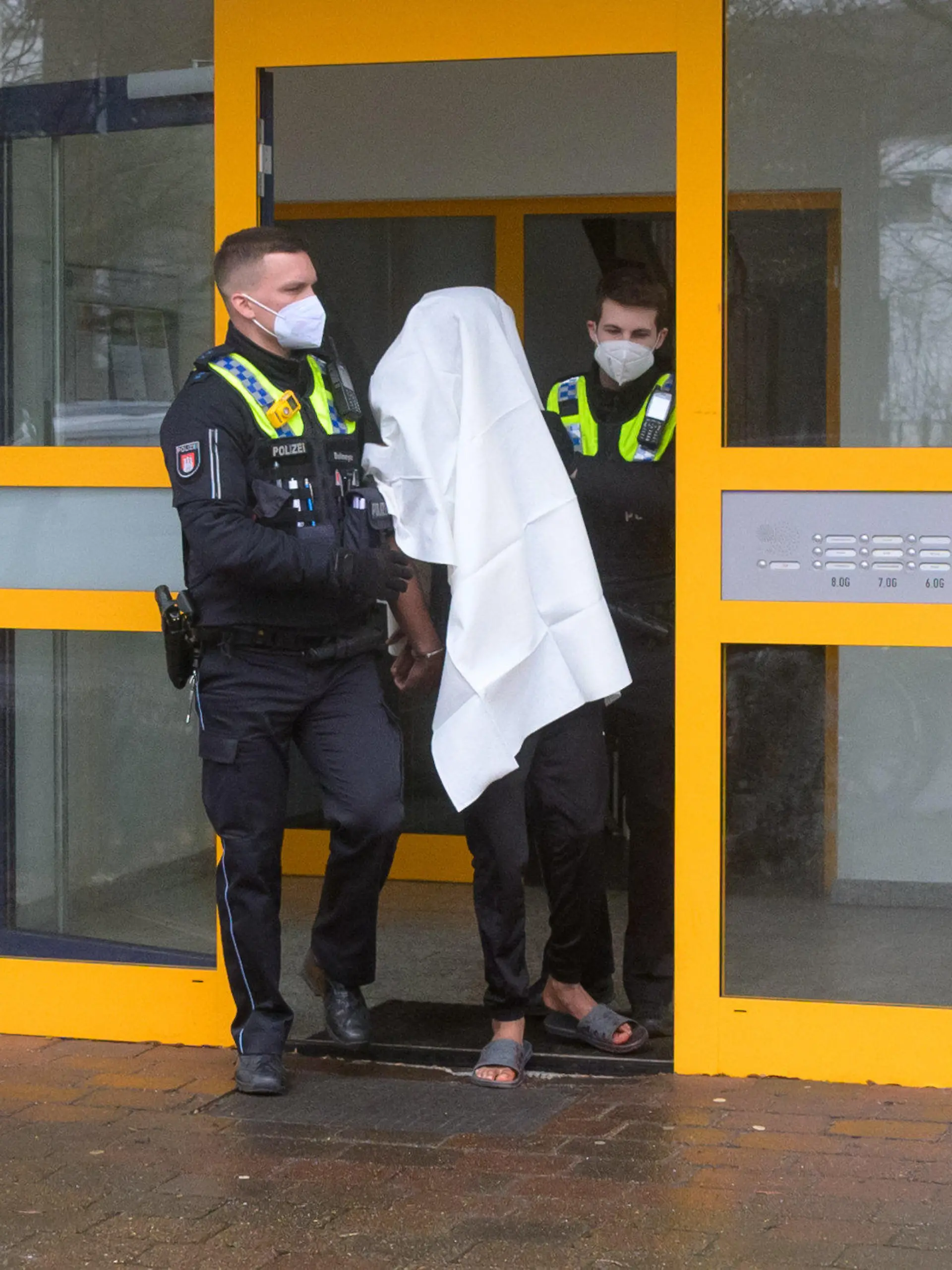 20.02.2022, Hamburg: Polizisten führen einen Tatverdächtigen in Handschellen aus dem Haus. Eine Frau ist am Sonntag mit lebensgefährlichen Stichverletzungen in Hamburg-Niendorf aufgefunden worden. Nach Angaben eines Sprechers hatte eine Anwohnerin Blut im Hausflur gesehen und die Einsatzkräfte verständigt. Den ersten Angaben zufolge sei von einer Auseinandersetzung die Rede gewesen, bei der eine Frau mit einem Messer verletzt worden sei. Foto: Jonas Walzberg/dpa +++ dpa-Bildfunk +++