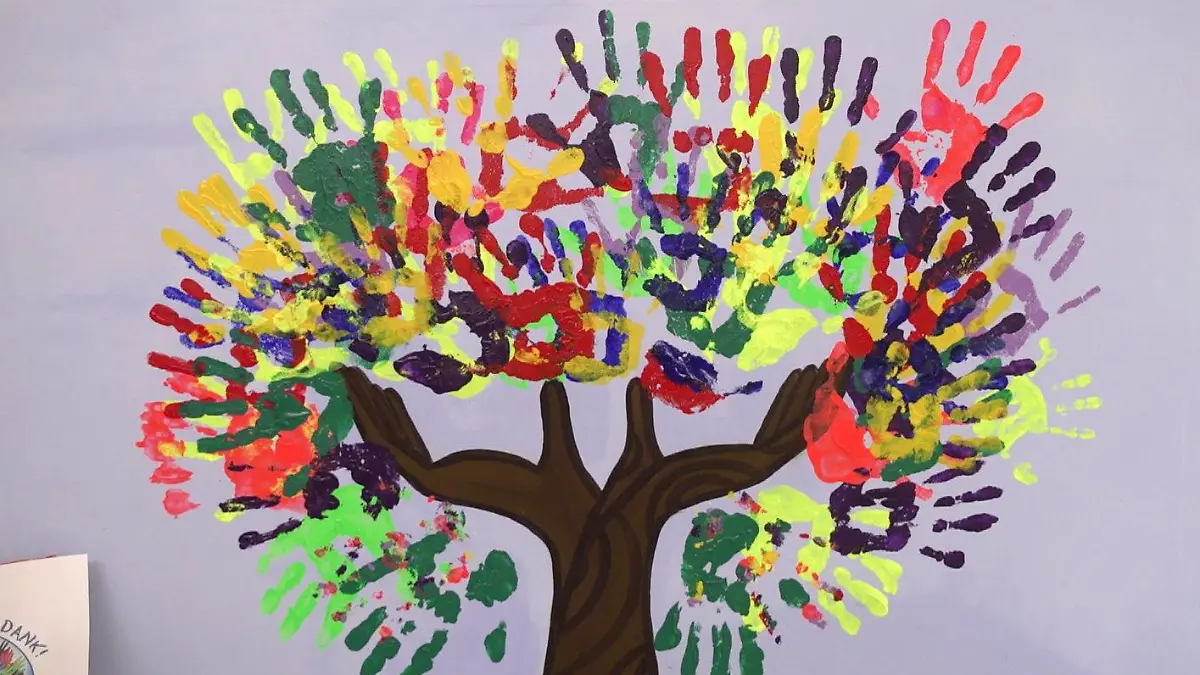 Bunte Handabrücke von Kindern auf einer weißen Leinwand mit einem braunen Baumstamm bilden gemeinsam eine bunte Baumkrone.