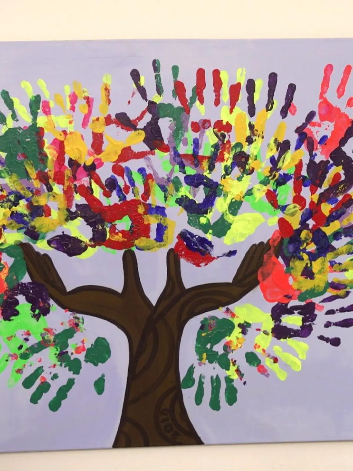 Bunte Handabrücke von Kindern auf einer weißen Leinwand mit einem braunen Baumstamm bilden gemeinsam eine bunte Baumkrone.