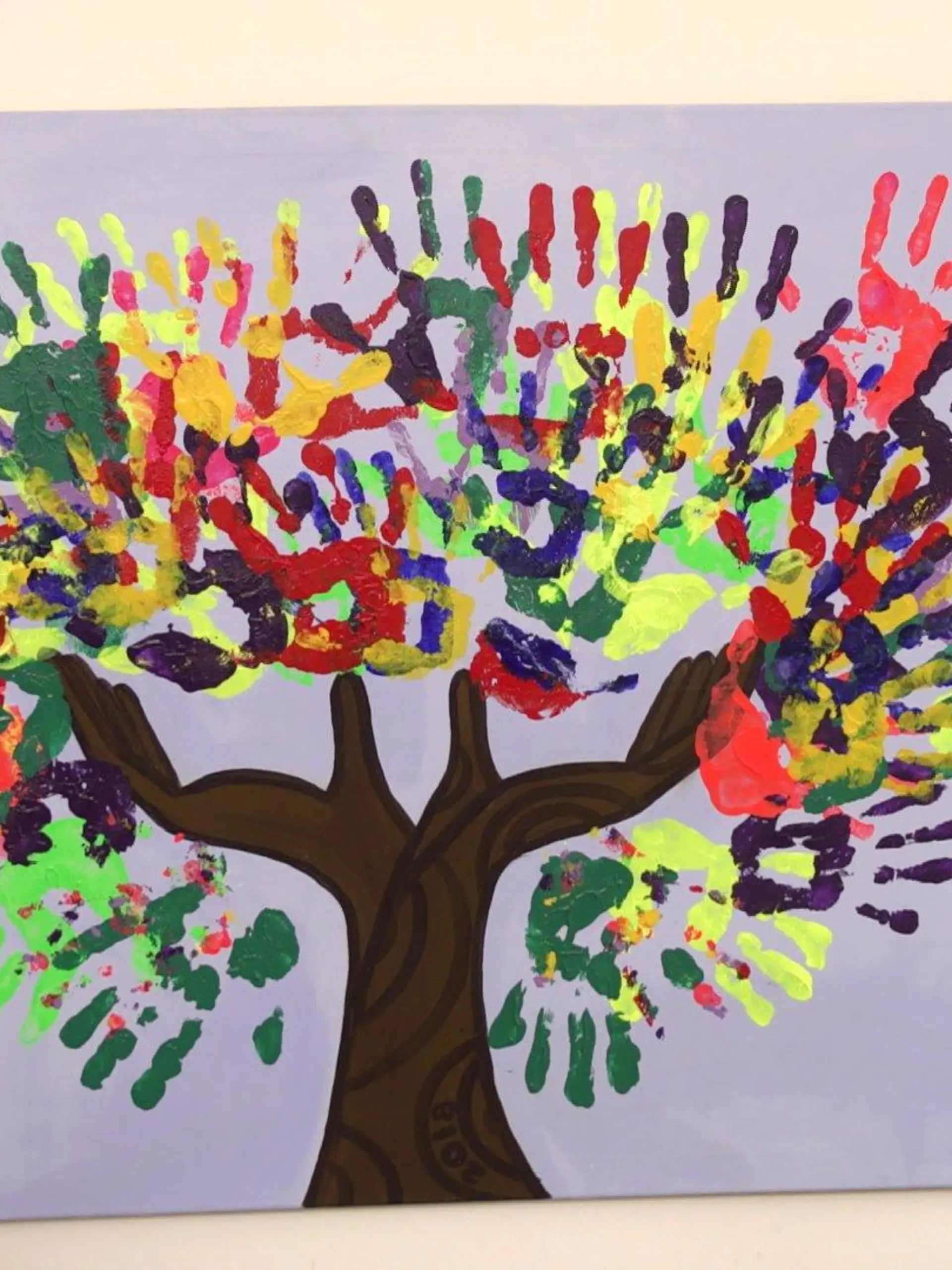 Bunte Handabrücke von Kindern auf einer weißen Leinwand mit einem braunen Baumstamm bilden gemeinsam eine bunte Baumkrone.