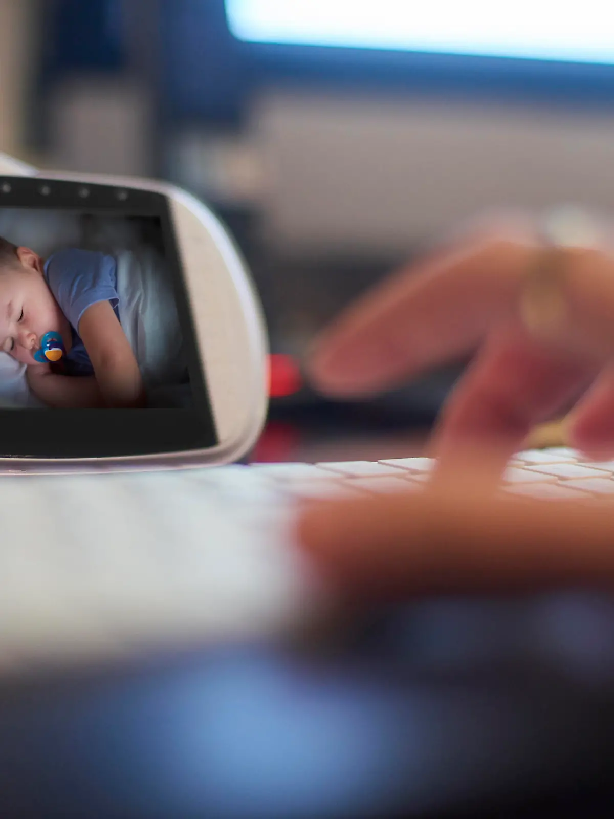 Baby monitor on the desk in home office. Parent is getting on with some work as the baby sleeps.